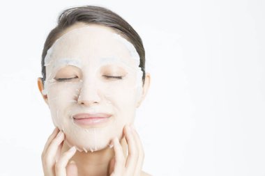 Beyaz arka planda maske takan güzel bir Asyalı kadın. Cilt bakımı kavramı