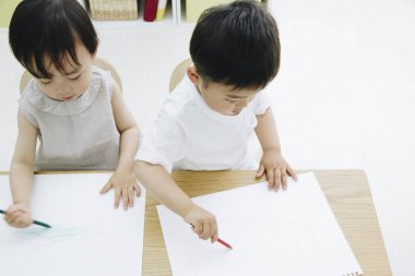 İki küçük Asyalı çocuk kağıda resim çiziyor. 