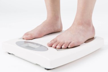 Kadın bacakları zemin terazisine basıyor, yakın plan. Terazinin üzerinde duran çıplak kadın, beyaz arkaplan