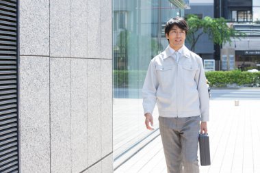 Yakışıklı Asyalı iş adamı evrak çantası tutuyor ve sokakta yürüyor. 