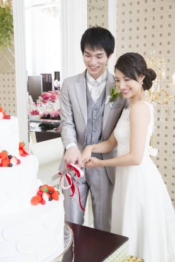 Mutlu genç Japon gelin ve damat düğün pastasını kesiyor.