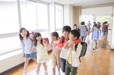 Okul koridorunda sırt çantalı bir grup Japon çocuk yürüyor. 