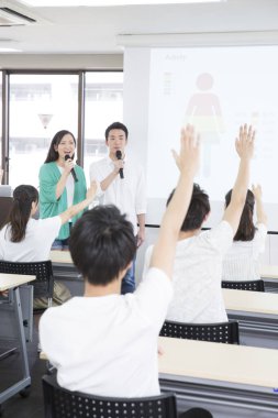 Ders sırasında mikrofonlu Asyalı öğrenciler sunum yapıyor