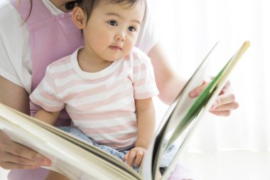 Asyalı anaokulu öğretmeni ve odada kitap okuyan sevimli küçük kız.