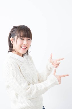 Beyaz kazaklı genç Japon kadın beyaz stüdyo geçmişini işaret ediyor.