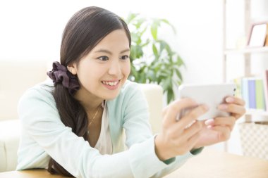Asyalı bir kadın cep telefonuyla evde fotoğraf çekiyor.