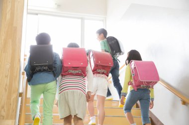 Okulda merdivenlerde yürüyen sırt çantalı bir grup Japon çocuk.
