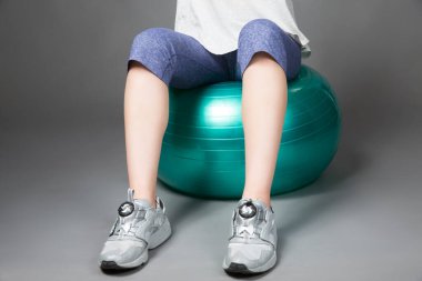 Spor salonunda yeşil topta oturan kadın.