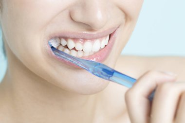 Genç kadın mavi arka plan üzerinde diş fırçalama 