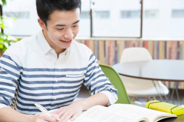 Asyalı öğrenci üniversitede masada okuyor. 