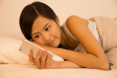 Asyalı kadın yatak odasında akıllı telefon kullanıyor. 