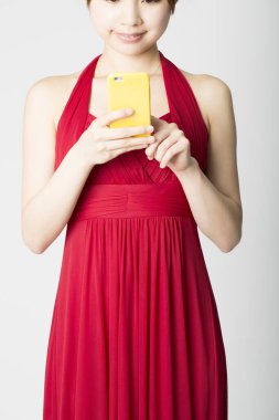 Sarı çantada cep telefonu tutan kırmızı elbiseli genç bir kadın.