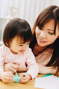 Anne ve kızı origami oyuncağı yapıyor. 