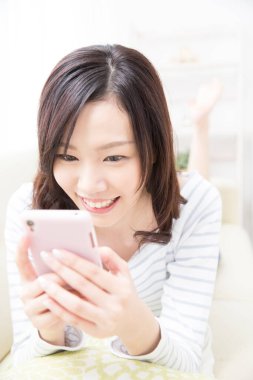 Güzel Asyalı kadın evde akıllı telefon kullanıyor.