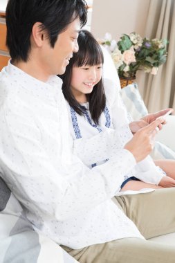 Gülümseyen baba ve kızı evde akıllı telefon kullanıyor.