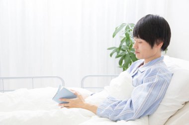 Hastanedeki yatakta kitap okuyan bir adam. 