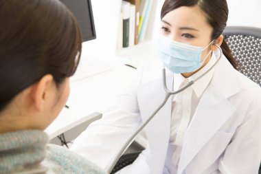 Steteskoplu kadın doktor klinikte hastayı kontrol ediyor.