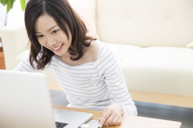 Genç Asyalı kadın oturma odasında dizüstü bilgisayar kullanıyor.