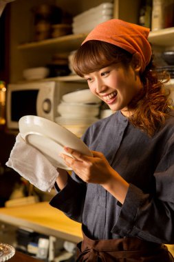 Asyalı garson kadın tabak siliyor.