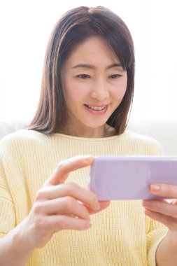 Asyalı kadın evde akıllı telefon kullanıyor. 