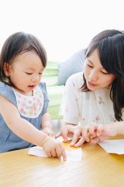 Anne ve kızı kağıtlarla oynuyor. 