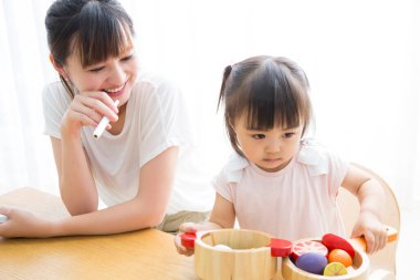 Anne kızının tahta oyuncaklarla oynamasını izliyor.