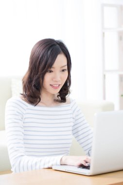 Evde dizüstü bilgisayar kullanan gülümseyen Asyalı kadın.