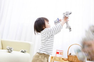 Küçük Asyalı kız evde gazetelerle oynuyor.