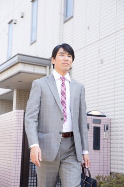 Takım elbiseli genç Japon işadamı evden ayrılıyor.