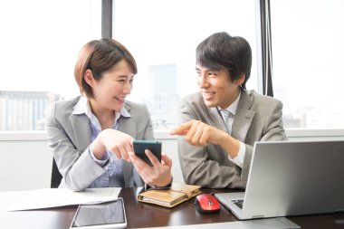 Asyalı iş adamları dizüstü bilgisayar kullanıyor ve cep telefonu tutuyorlar.