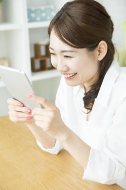 Genç Asyalı kadın oturma odasında tablet kullanıyor.