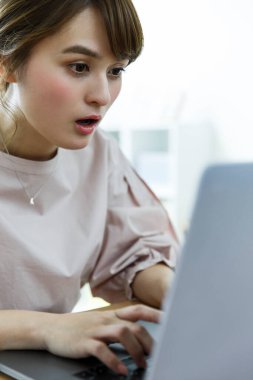 Genç Asyalı kadın modern bir dairede dizüstü bilgisayar kullanıyor.