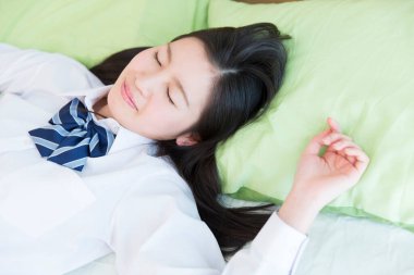 Üniformalı, yorgun Asyalı genç kız yatakta uyuyor.