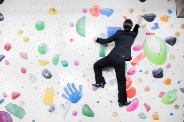 Takım elbiseli güzel Japon kadın spor salonunda duvara tırmanıyor. 