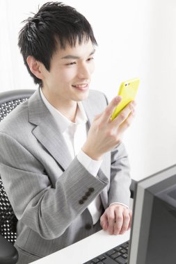 Genç Asyalı işadamı ofiste akıllı telefon kullanıyor.