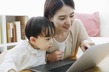 Asyalı anne ve küçük kızı evde dizüstü bilgisayar kullanıyorlar.