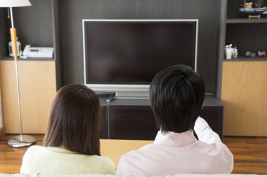 Genç Asyalı çift evde dinlenip oturma odasında televizyon seyrediyor.
