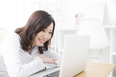 Evde dizüstü bilgisayar kullanan gülümseyen Asyalı kadın.