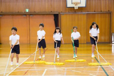 Okuldaki spor salonunu temizleyen bir grup çocuk.