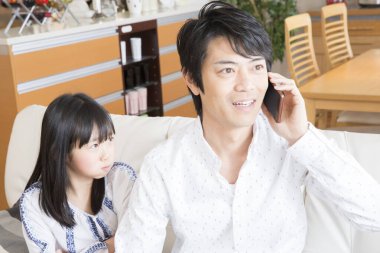 Asyalı baba telefonda konuşuyor ve kızı onu dinliyor. 