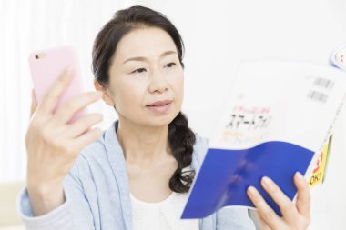 Bir mesaj okurken kitap okuyan Asyalı genç kadın. 