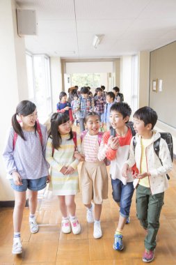 Okul koridorunda sırt çantalı bir grup Japon çocuk yürüyor. 