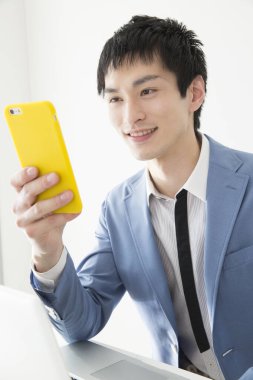 Ofiste akıllı telefon kullanan genç Japon iş adamının yakın plan portresi.