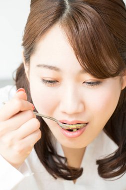 Genç Asyalı kadın kaşıkla çorba içiyor.