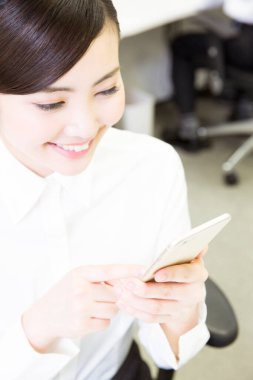 Genç Asyalı iş kadını ofiste akıllı telefon kullanıyor. 