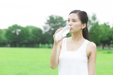 Yeşil yaz parkında gündüz vakti su içen güzel Japon kadın. 
