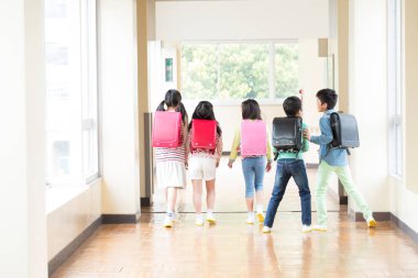 Okul koridorunda sırt çantalı bir grup Japon çocuk yürüyor. Arka plan