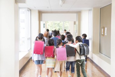 Okul koridorunda sırt çantalı bir grup Japon çocuk yürüyor. Arka plan
