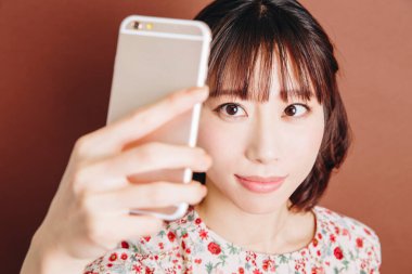 Asyalı kadın cep telefonuyla selfie çekiyor.