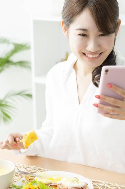 Kadın mutfakta yemek yerken cep telefonu kullanıyor.